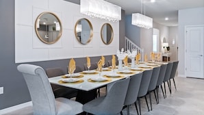 A dining area with a long table set for a meal, grey chairs, and three round mirrors on the wall. - Last Minute Disney! Private Pool, Hot Tub, Game Room & Themed Bedrooms. Book Now! #78231 (Orlando)