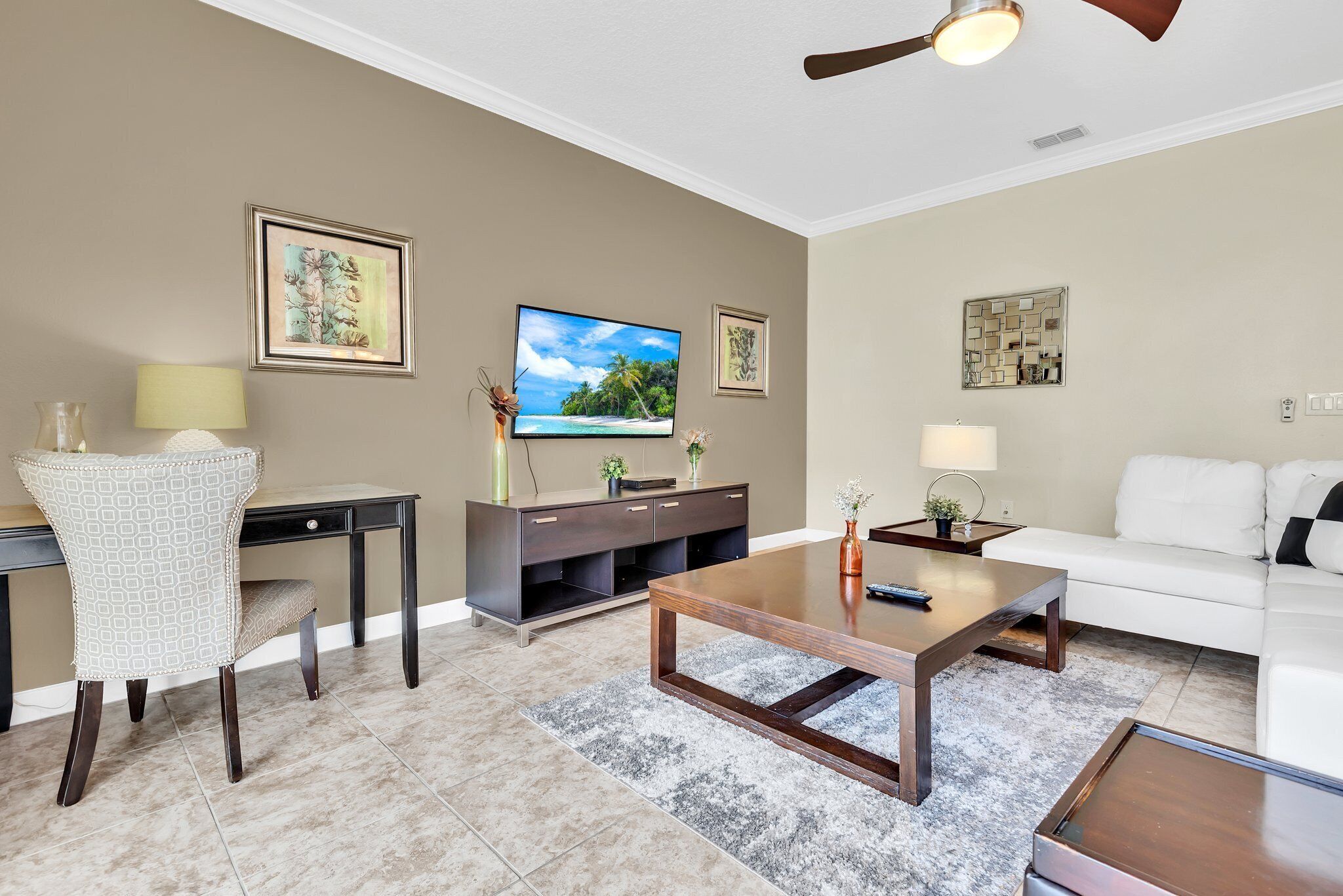 A living room with a TV, a white sofa, a coffee table, a dining table, and a chair.