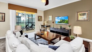 A modern living room with a sofa, coffee table, TV, and a balcony with outdoor seating. - Last Minute Disney Getaway! Private Pool, Hot Tub & Game Room. Book Now! #82571 (Orlando)
