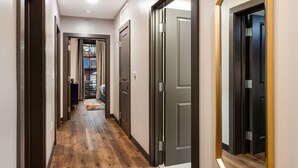 Un pasillo con suelo de madera, puertas oscuras y vistas a una habitación con cama y ventana.