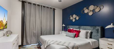 A bedroom with a bed, a ceiling fan, a nightstand, a lamp, and a wall decoration.