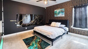 Quarto com cama, ventoinha no teto, obras de arte nas paredes e janela com cortinas.