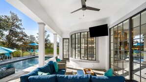 Un espacio exterior cubierto con piscina, mobiliario de mimbre y un televisor de pantalla plana.