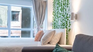 Um quarto moderno com uma janela grande, cama com roupa de cama branca, sofá cinza e manta verde.