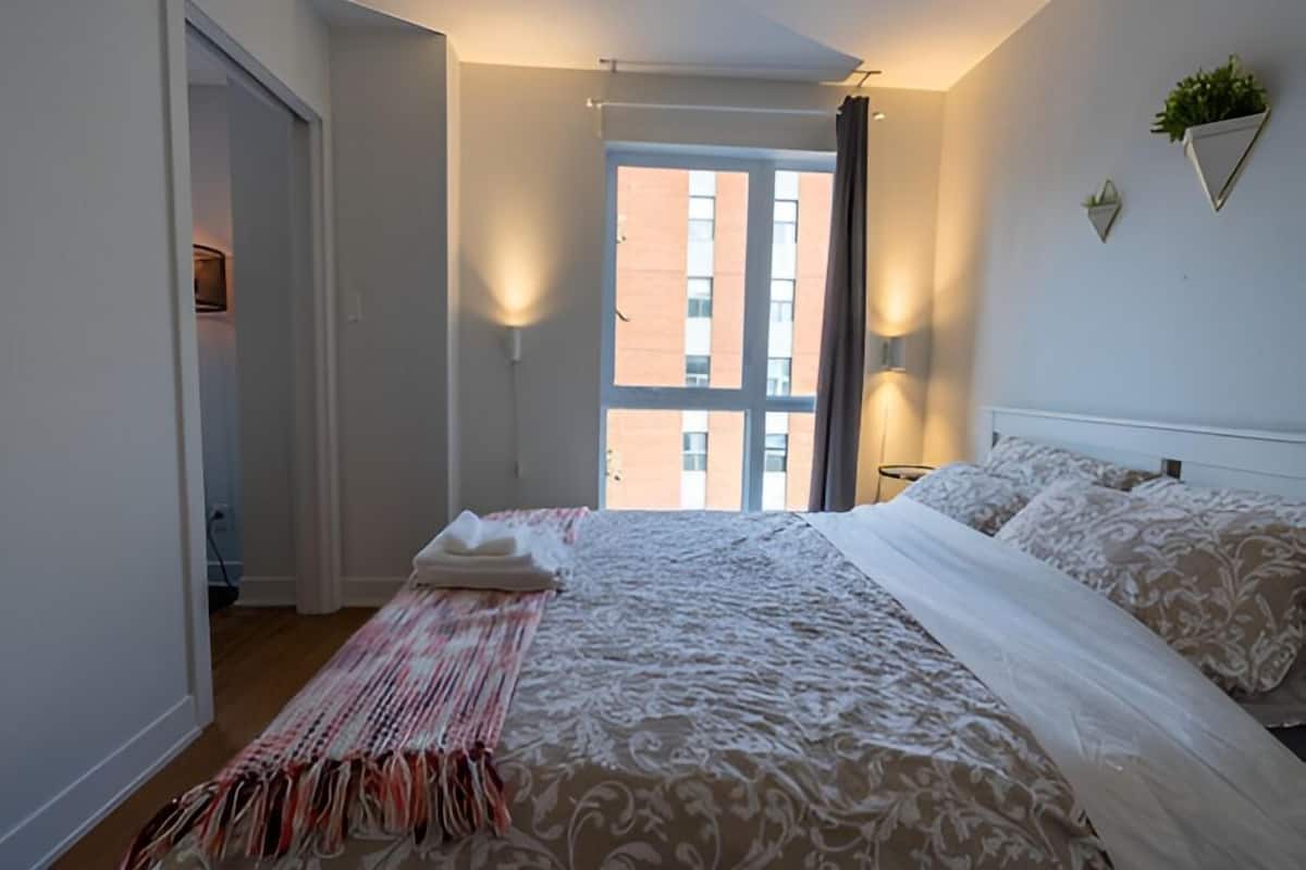 Une chambre d’hôtel avec un grand lit, une vue sur un immeuble par la fenêtre et une porte donnant sur une autre pièce.