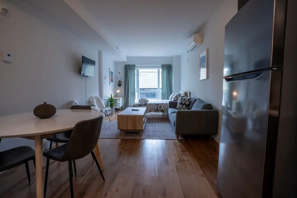 A modern living room with a dining area, a sofa, a coffee table, and a large refrigerator.