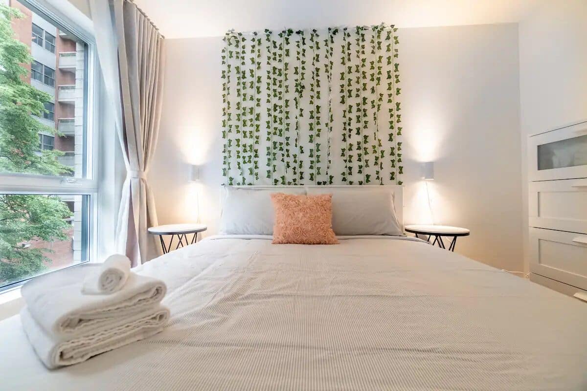 Une chambre d’hôtel avec un grand lit, deux tables de chevet, une télévision et une vue sur un bâtiment à l’extérieur.