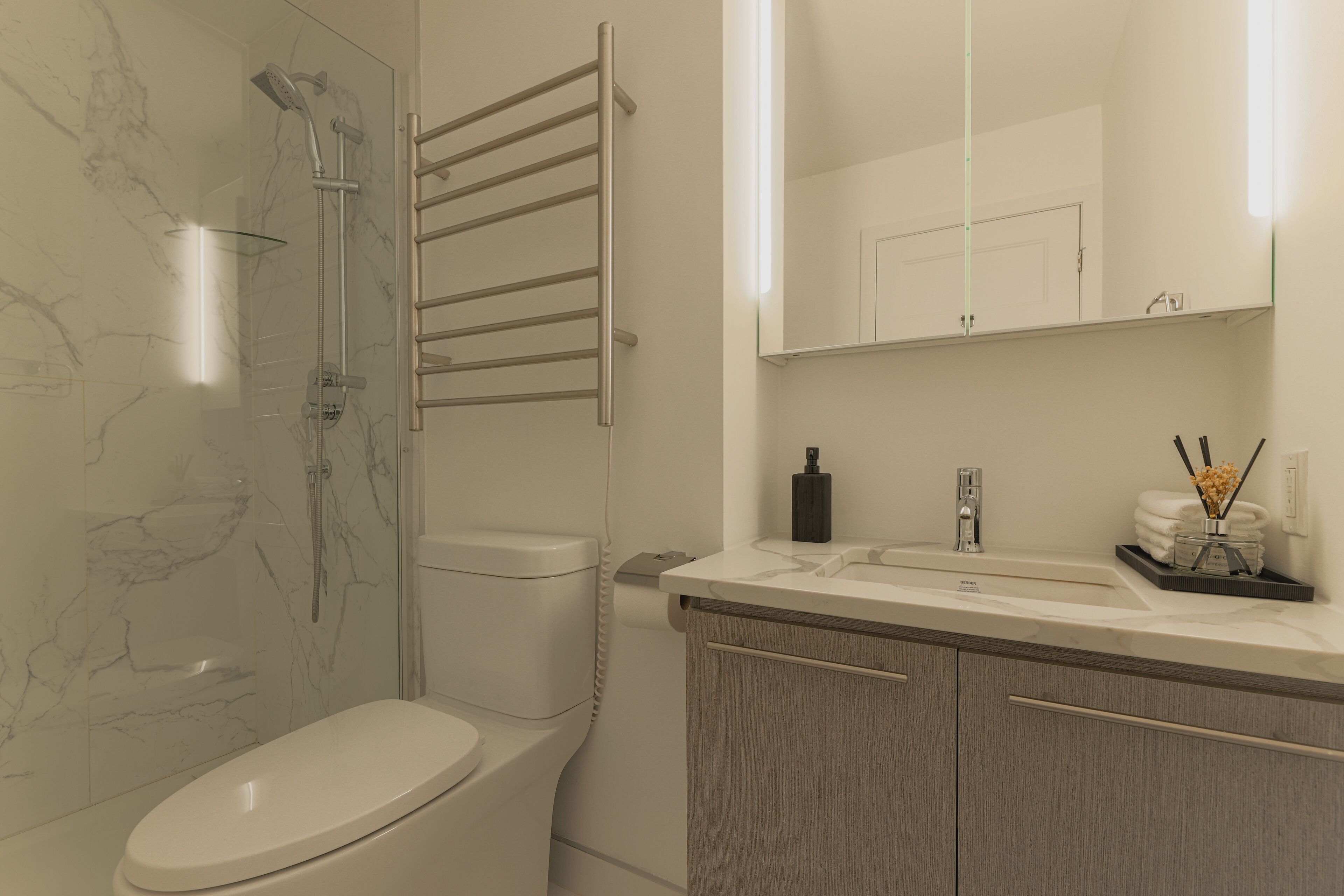Een moderne badkamer met een douchecabine van glas, een wit toilet, een wastafel met spiegel en een handdoekhouder.
