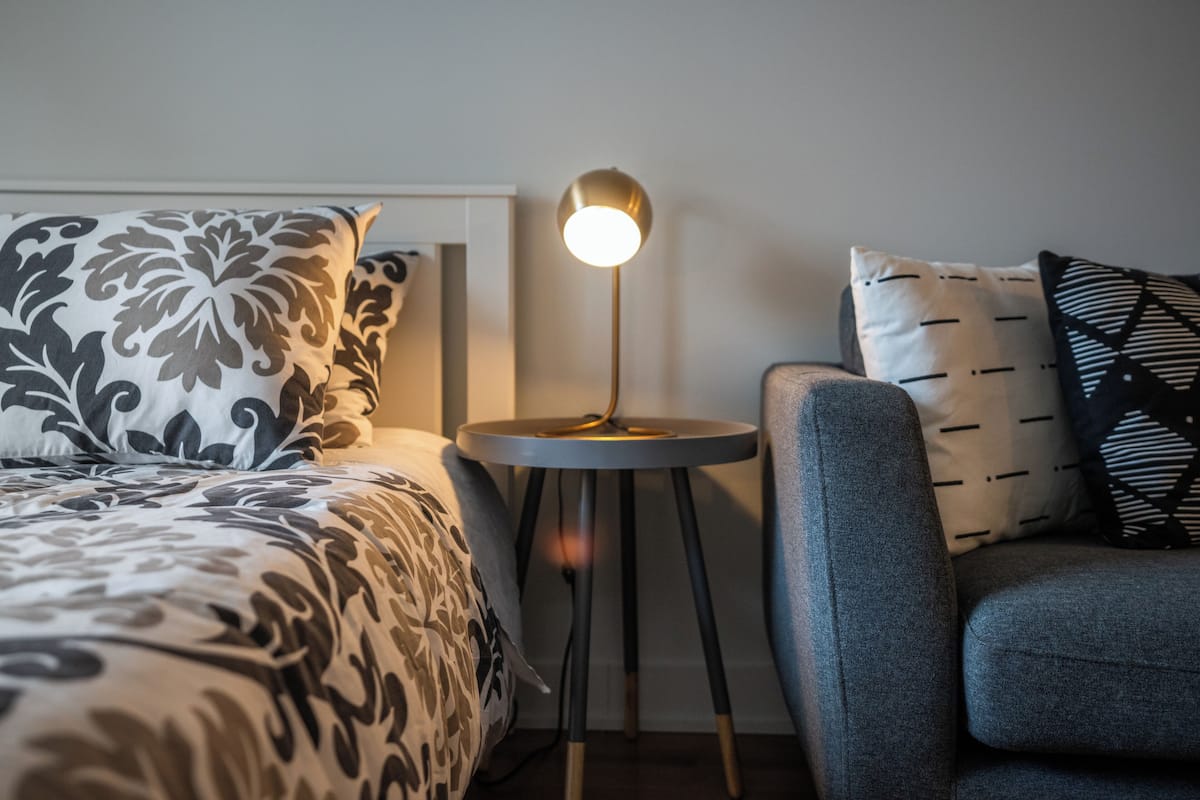 Une chambre bien rangée, avec un lit, une table de chevet dotée d’une lampe et un canapé.