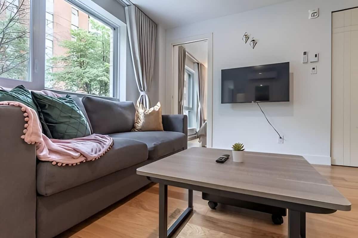 Un salon moderne avec un canapé gris, une table basse en bois et un téléviseur fixé au mur.