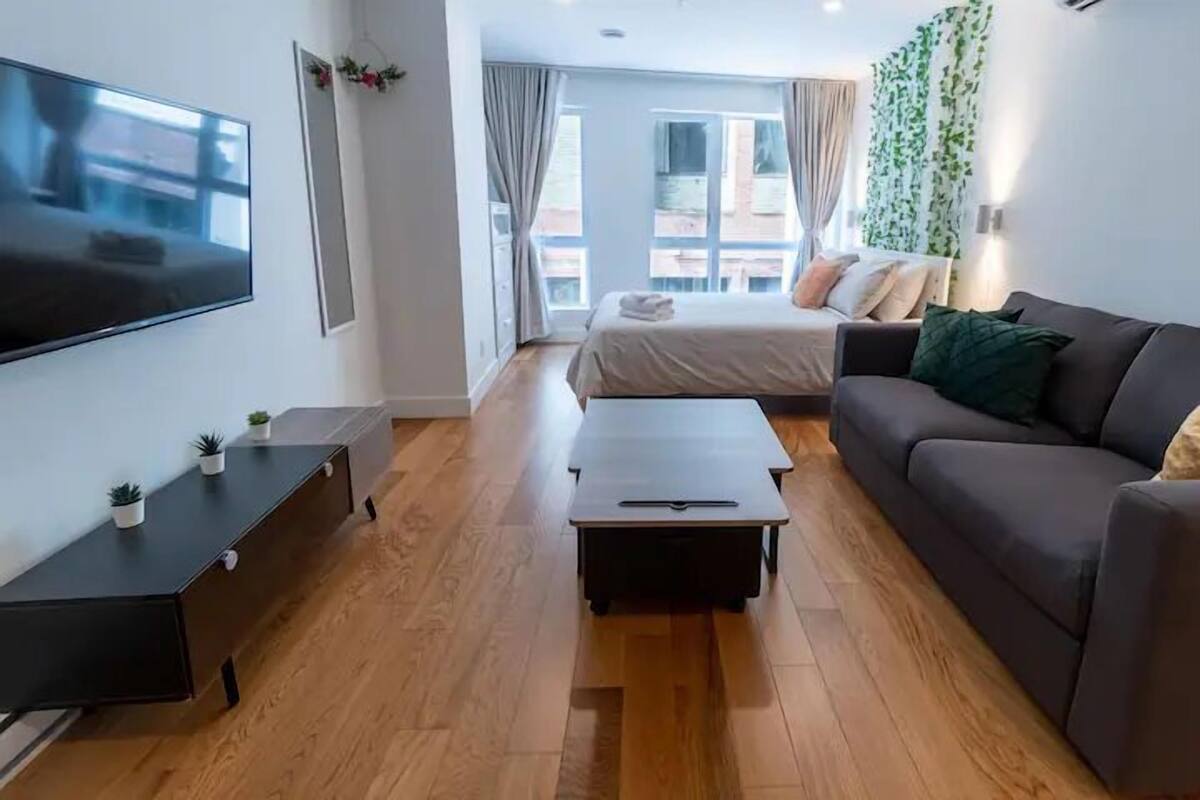 Une chambre d’hôtel moderne équipée d’un lit, d’un canapé, d’une télévision, d’une petite table et d’une fenêtre avec des rideaux.