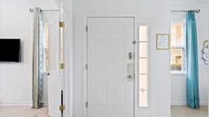 A room with a white door, a flat-screen TV on the wall, a window with blinds, and a teal curtain. - Last Minute Disney Getaway! Townhouse with Private Pool. Book Now! #87733 (Orlando)