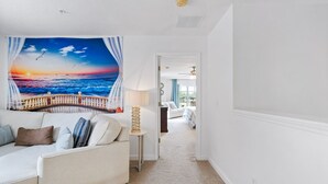 A hallway with a white wall, a beige carpet, a white sofa with cushions, a small table with a lamp, and a door leading to another room. - Last Minute Disney Getaway! Townhouse with Private Pool. Book Now! #87733 (Orlando)