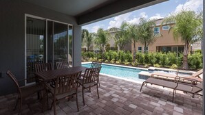 Portico coperto con piscina, mobili da esterno e vista su una zona residenziale con palme e un edificio.