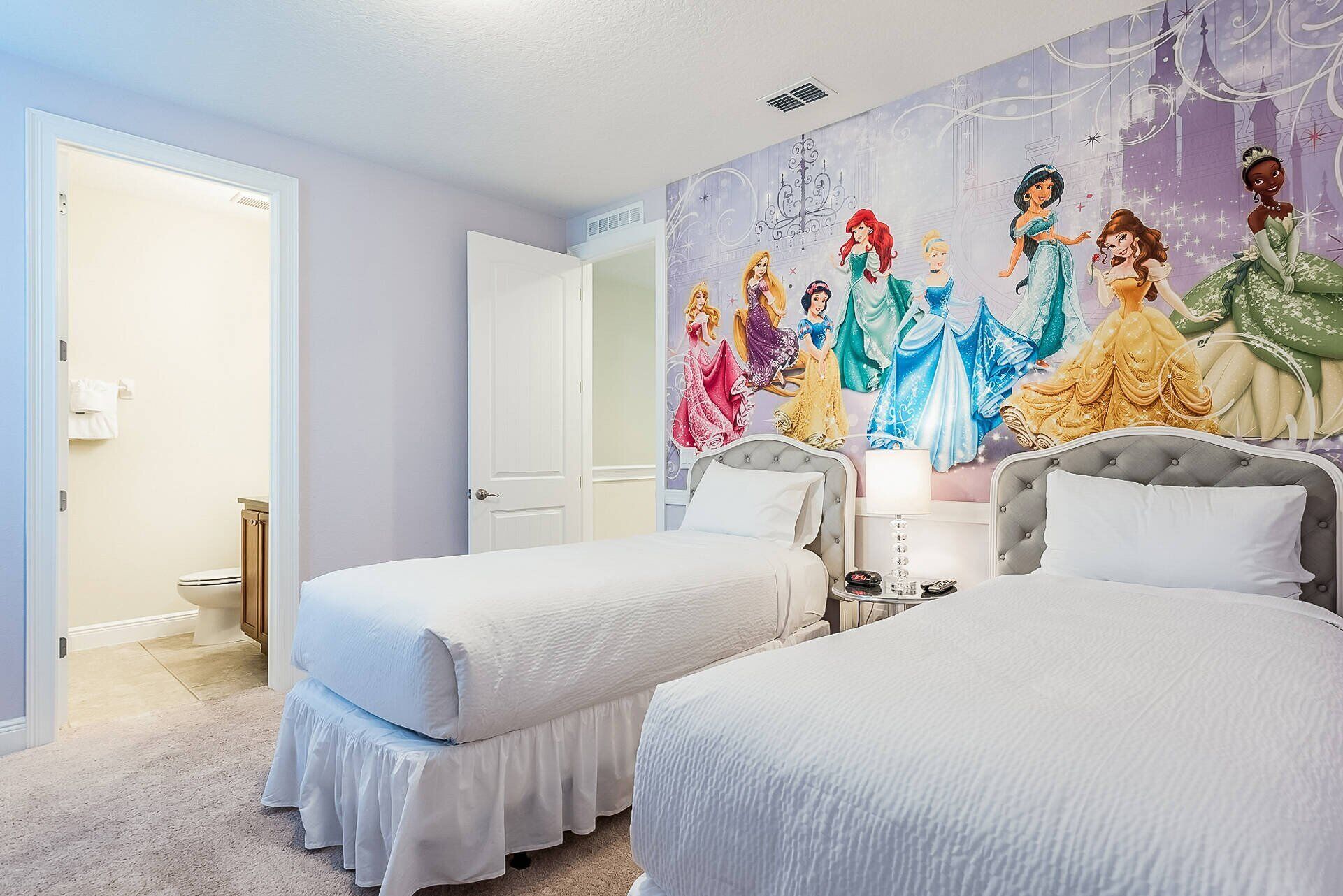 A bedroom with two beds, a large mural of Disney princesses, and a bathroom visible through an open door.