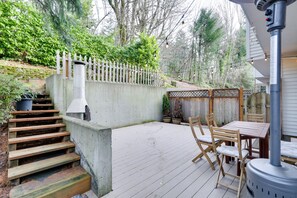 Une terrasse en bois avec une table et des chaises, un escalier en béton et une clôture blanche en bois.