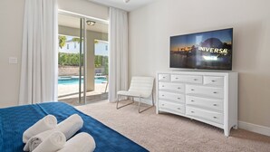 A hotel room with a bed, a TV, a white dresser, a chair, and a view of a swimming pool. - Last Minute Disney! Private Pool, Hot Tub, Game Room & Themed Bedrooms. Book Now! #89725 (Orlando)