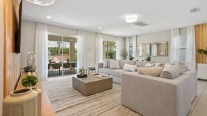 A modern living room with a grey sofa, a wooden coffee table, and a TV mounted on the wall. - Last Minute Disney! Private Pool, Hot Tub, Game Room & Themed Bedrooms. Book Now! #89725 (Orlando)