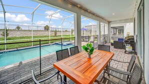 Un patio couvert avec une piscine, des sièges d’extérieur et un barbecue.