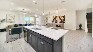 Una cocina moderna con una isla grande, iluminación colgante y un comedor con sofá y sillas.
