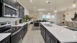 Una cocina moderna con una isla grande, armarios oscuros, electrodomésticos de acero inoxidable e iluminación colgante.