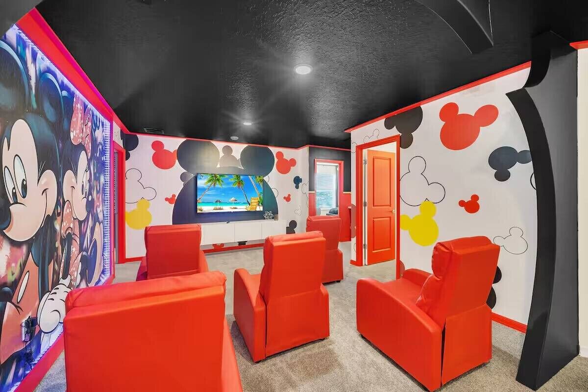 A room with red chairs, a TV, and Mickey Mouse-themed walls.