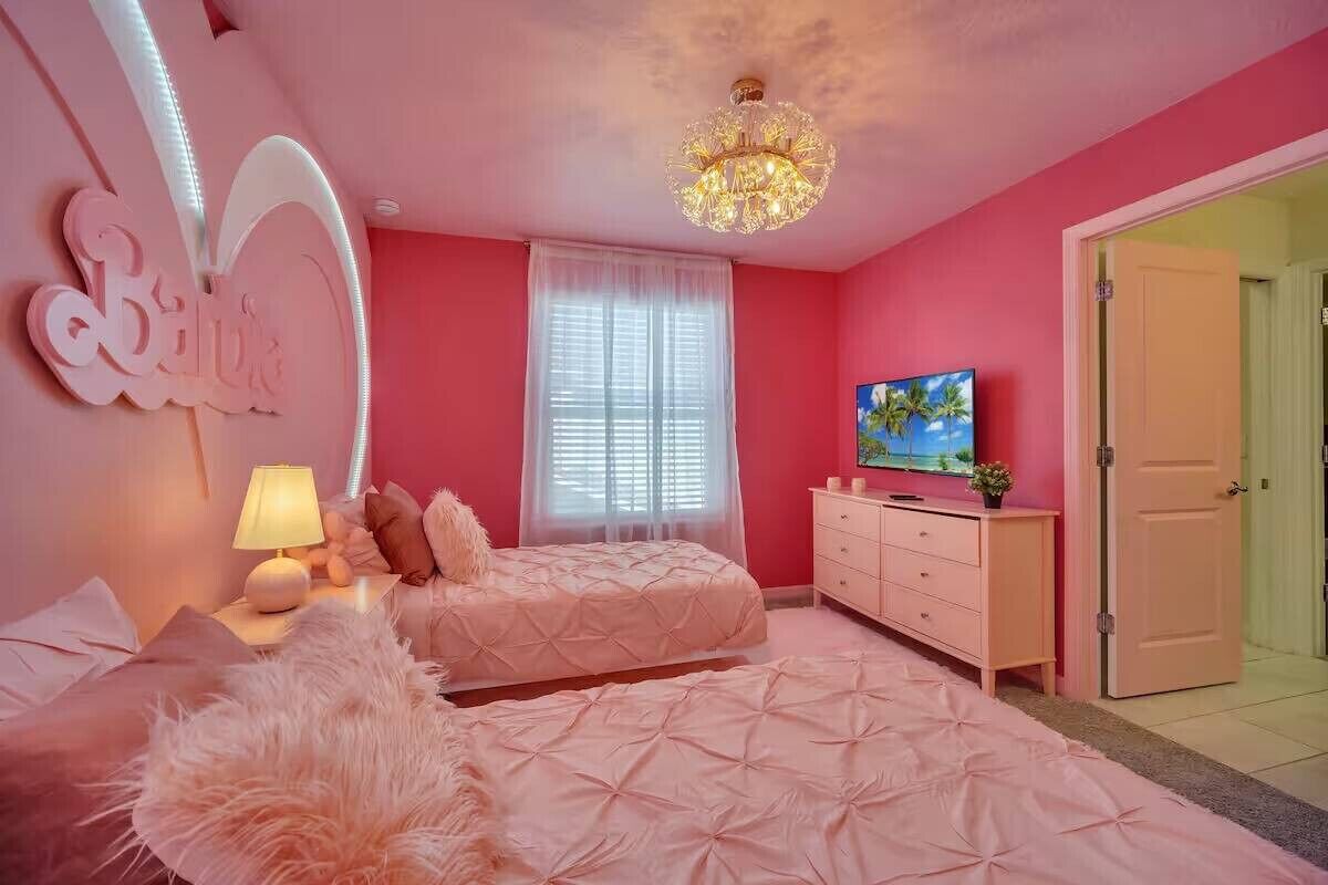 A pink-themed bedroom with a bed, a dresser, a TV, and a door.