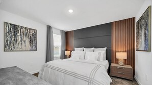Ein modernes Schlafzimmer mit einem großen Bett, zwei Nachttischen mit Lampen, einem Kopfteil aus vertikalen Holzleisten und abstrakter Kunst an den Wänden.