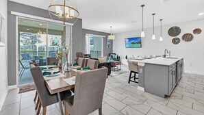 Une cuisine moderne dotée d’un îlot central, d’un coin repas agrémenté d’un lustre, et donnant par de grandes portes vitrées sur un patio extérieur.