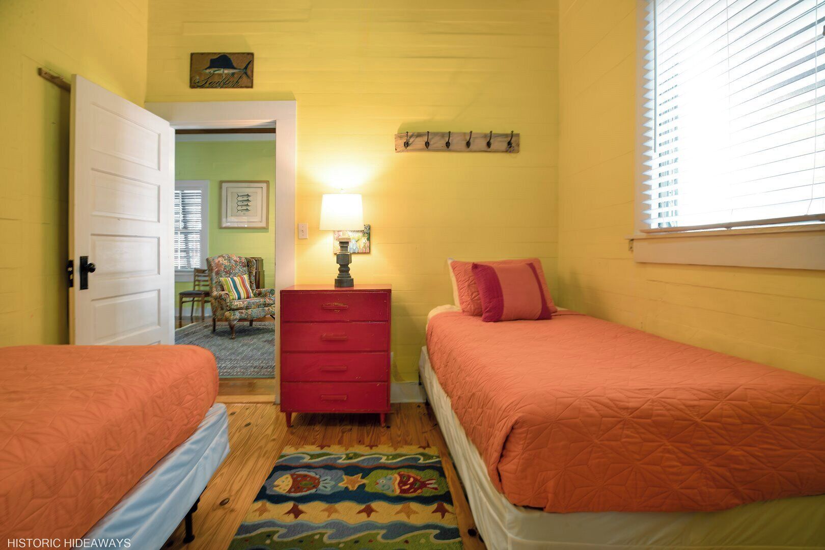 A room with two beds, a dresser, a lamp, and a chair.