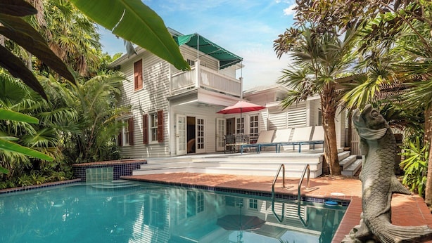 A pool area with a clear blue pool, a white building with a balcony, and a statue of a fish. - Truman House (Key West)