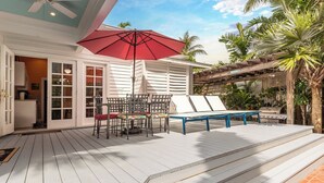 A covered outdoor patio with a red umbrella, a table with chairs, and a grill. - Truman House (Key West)