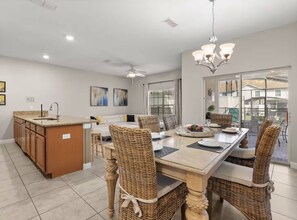 A modern kitchen with a dining area, featuring a central island, wicker chairs, and a chandelier.