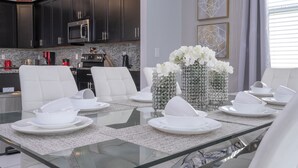 A modern dining area with a glass table set for six, surrounded by white chairs. - Last Minute Disney! Private Pool, Hot Tub & Themed Bedrooms. Book Now! #93745 (Orlando)