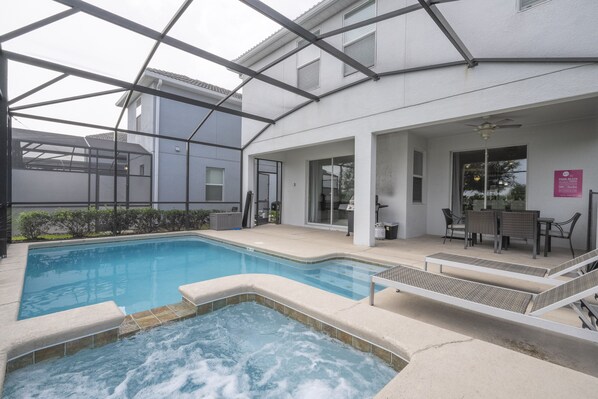 Una piscina con jacuzzi, mobiliario exterior y un patio cubierto.