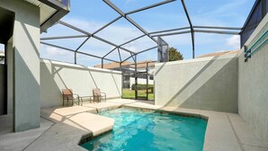 Piscina interior con techo de cristal, dos sillones de descanso y vista a una zona residencial.