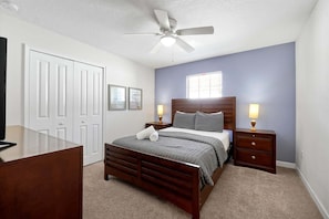 Quarto com cama, mesas de cabeceira, ventilador de teto, janela e porta.