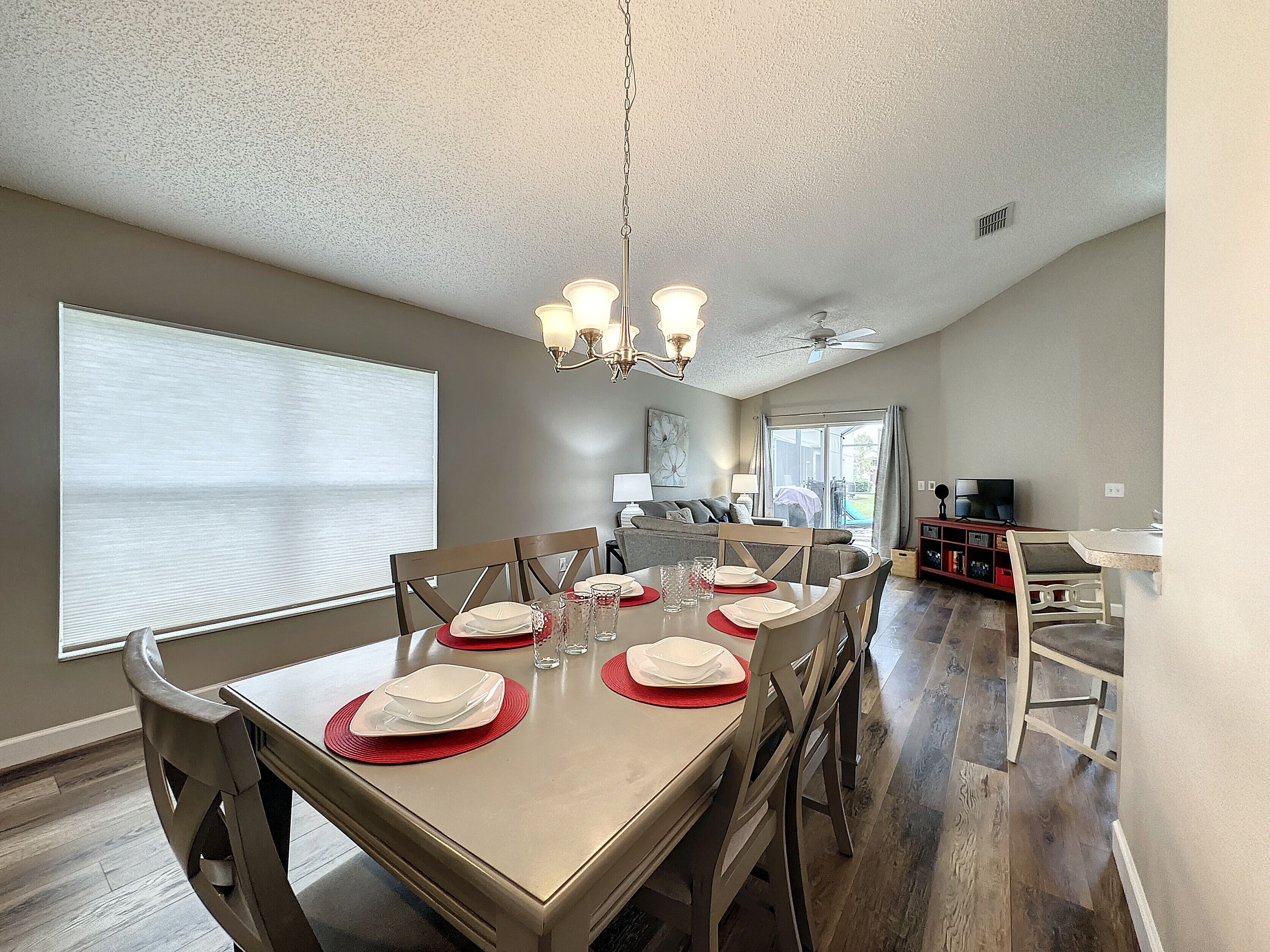 A dining area with a table set for six, a chandelier, and a view of the living room.