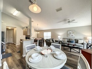 A modern living room with a dining area, featuring a round table set for four, a sofa set, and a ceiling fan.