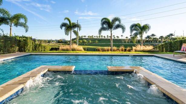 Piscina con jacuzzi, rodeada de palmeras y césped.