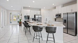 Una cocina moderna con armarios blancos, electrodomésticos de acero inoxidable y una isla central con taburetes de bar.