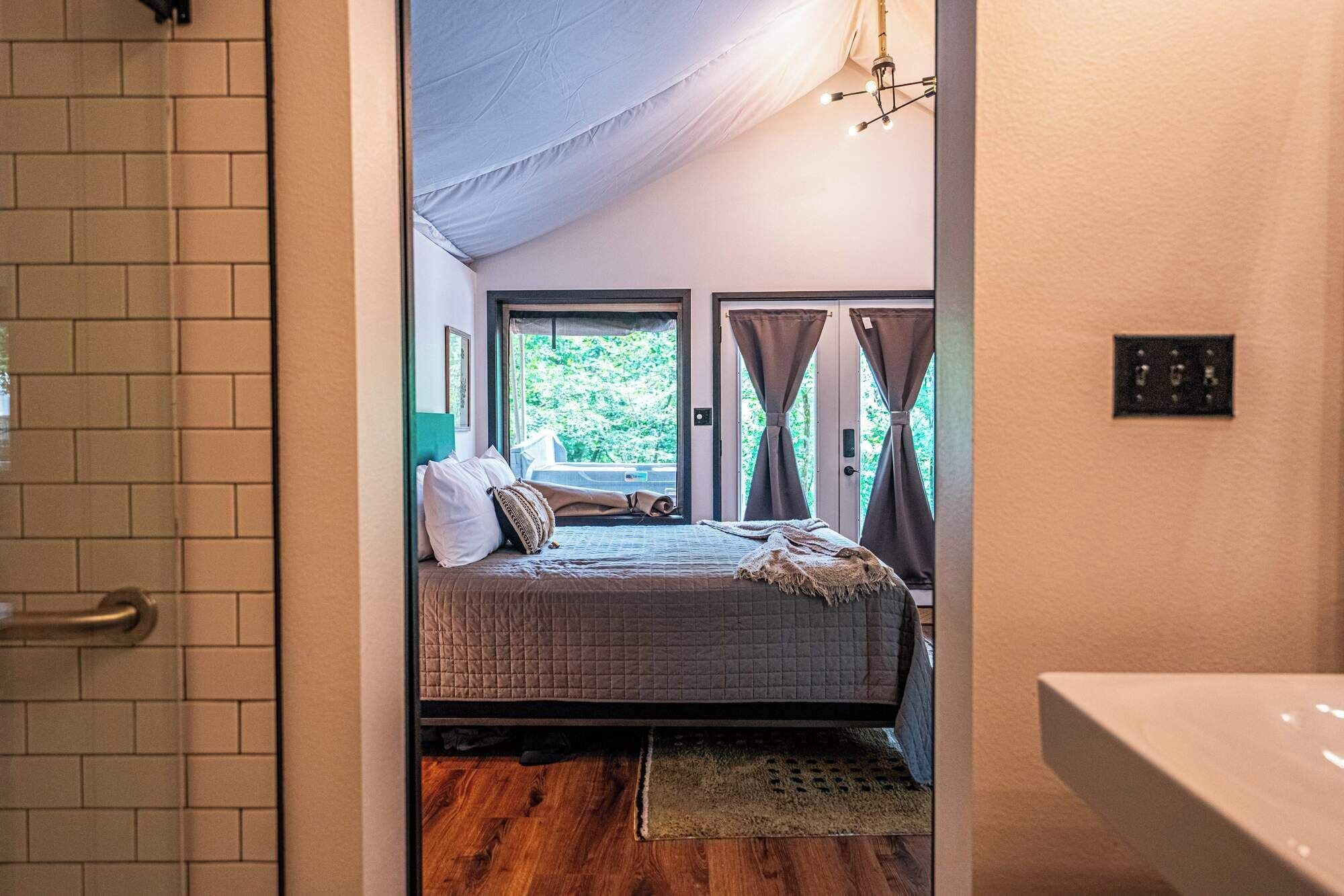 Un dormitorio con cama, ventana con cortinas, suelo de madera y una lámpara en el techo.
