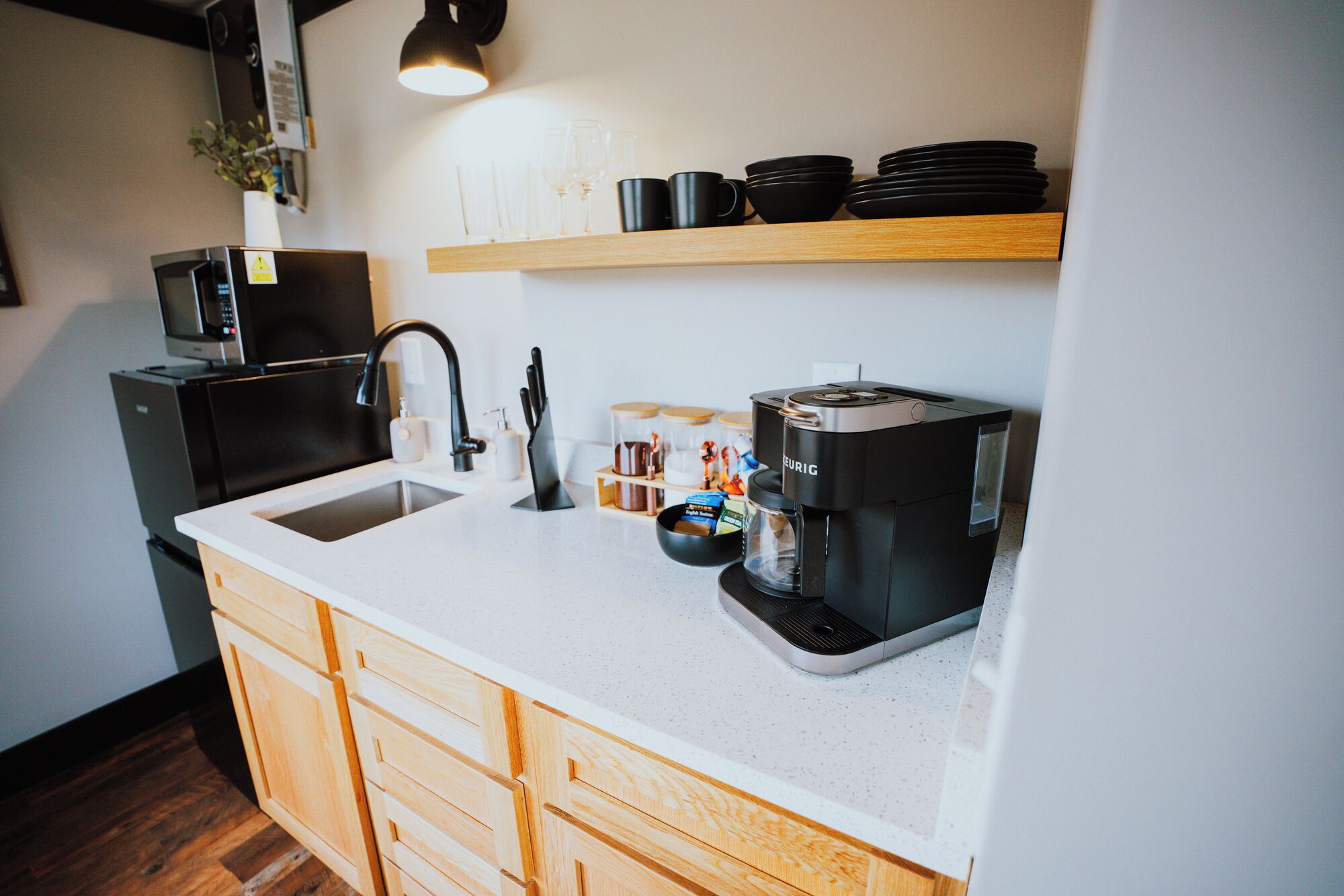 A modern kitchen with a white countertop, a black coffee maker, and a microwave above the sink.