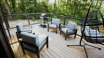 Eine Terrasse mit Gartenmöbeln, darunter Stühle und ein Hängesessel, umgeben von einer Holzterrasse und einem Metallgeländer.