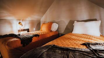 Two beds with orange bedding, a wooden headboard, and a hanging light fixture in a room with sloped ceilings.