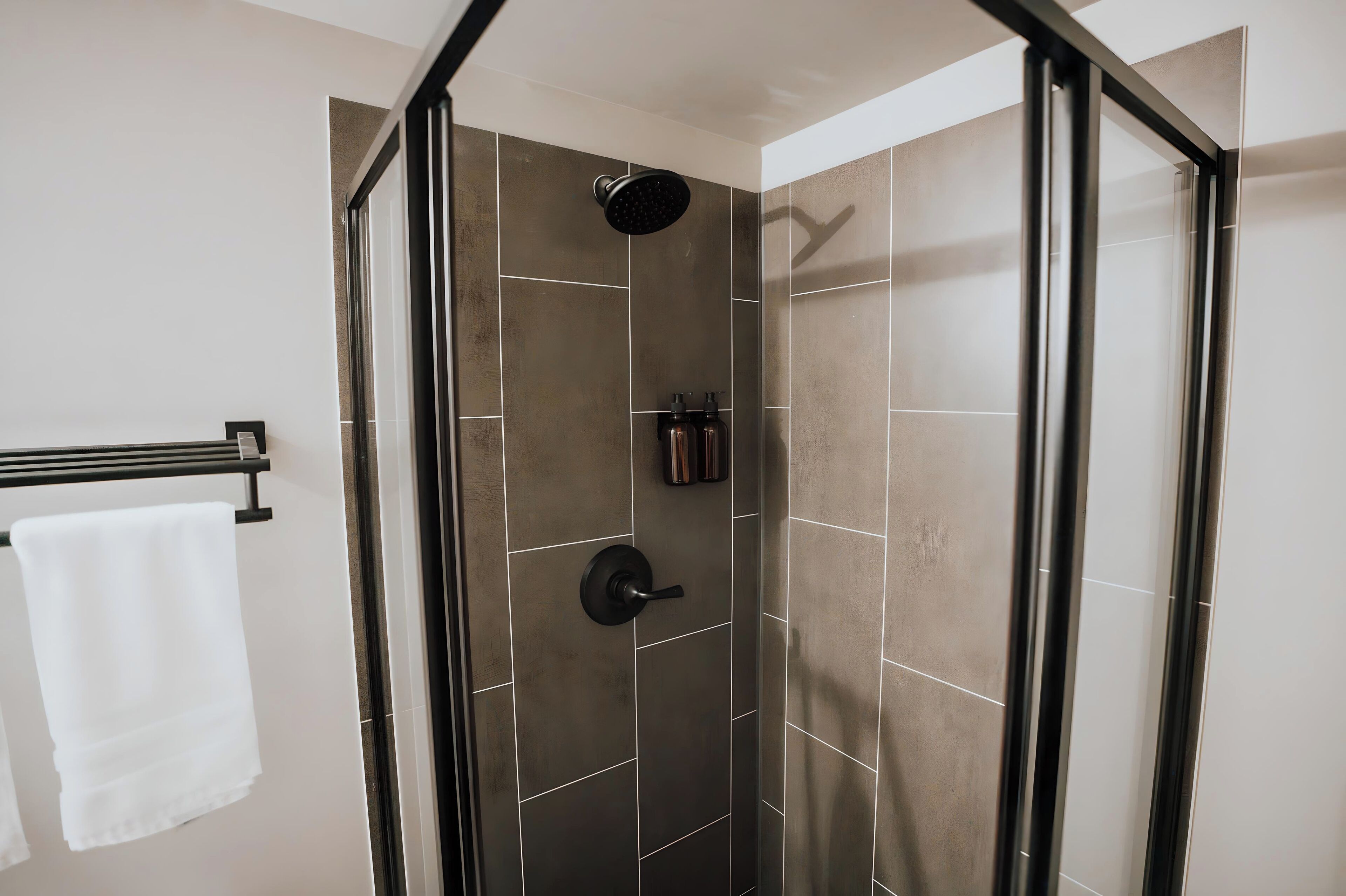 Une douche à l’italienne avec une porte en verre, des murs carrelés et un porte-serviettes sur lequel est posée une serviette blanche.