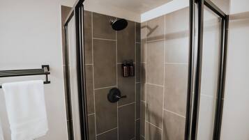Une douche à l’italienne avec une porte en verre, des murs carrelés et un porte-serviettes sur lequel est posée une serviette blanche.