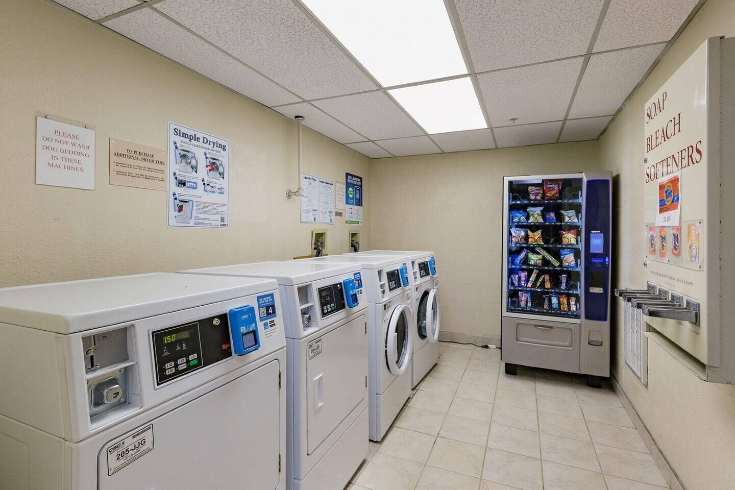 Een wasserette met meerdere wasmachines en drogers, een automaat met snacks, en borden met wasinstructies.