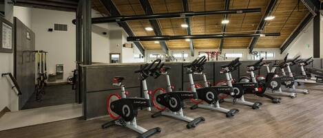 A gym with multiple stationary bikes, a wooden ceiling, and a counter with exercise equipment.