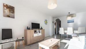 Una sala de estar moderna con un televisor de pantalla plana, un mueble de madera, comedor y un amplio ventanal.